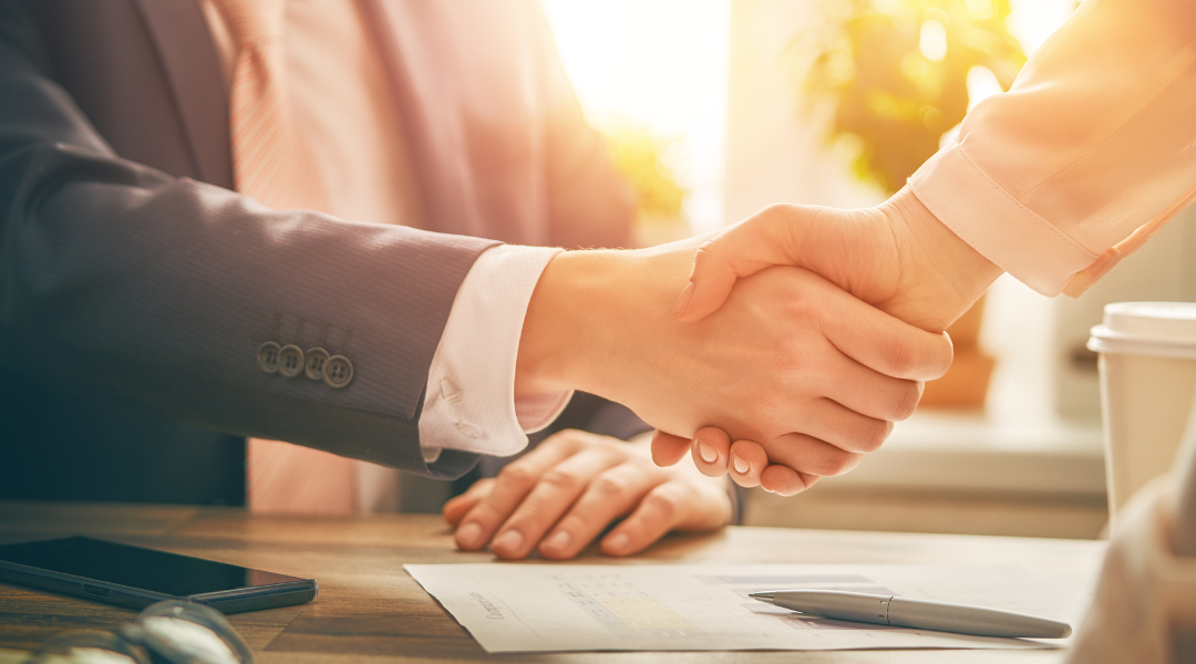 Two business professionals shaking hands over a desk, symbolizing a successful collaboration between marketing and sales teams.